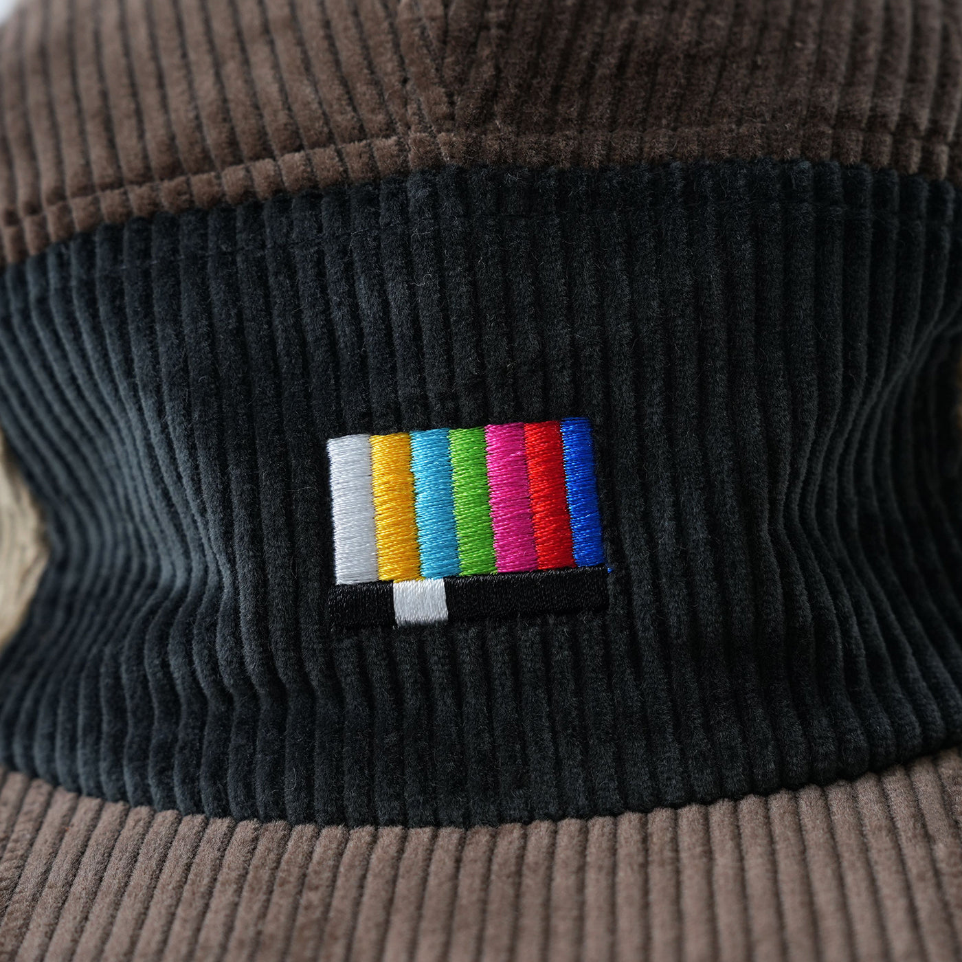 Close-up of a brown and black corduroy hat with a colorful TV colour test icon logo