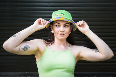 Woman wearing a green tank top and green corduroy bucket hat with colourful pattern on alternate side, against a dark background