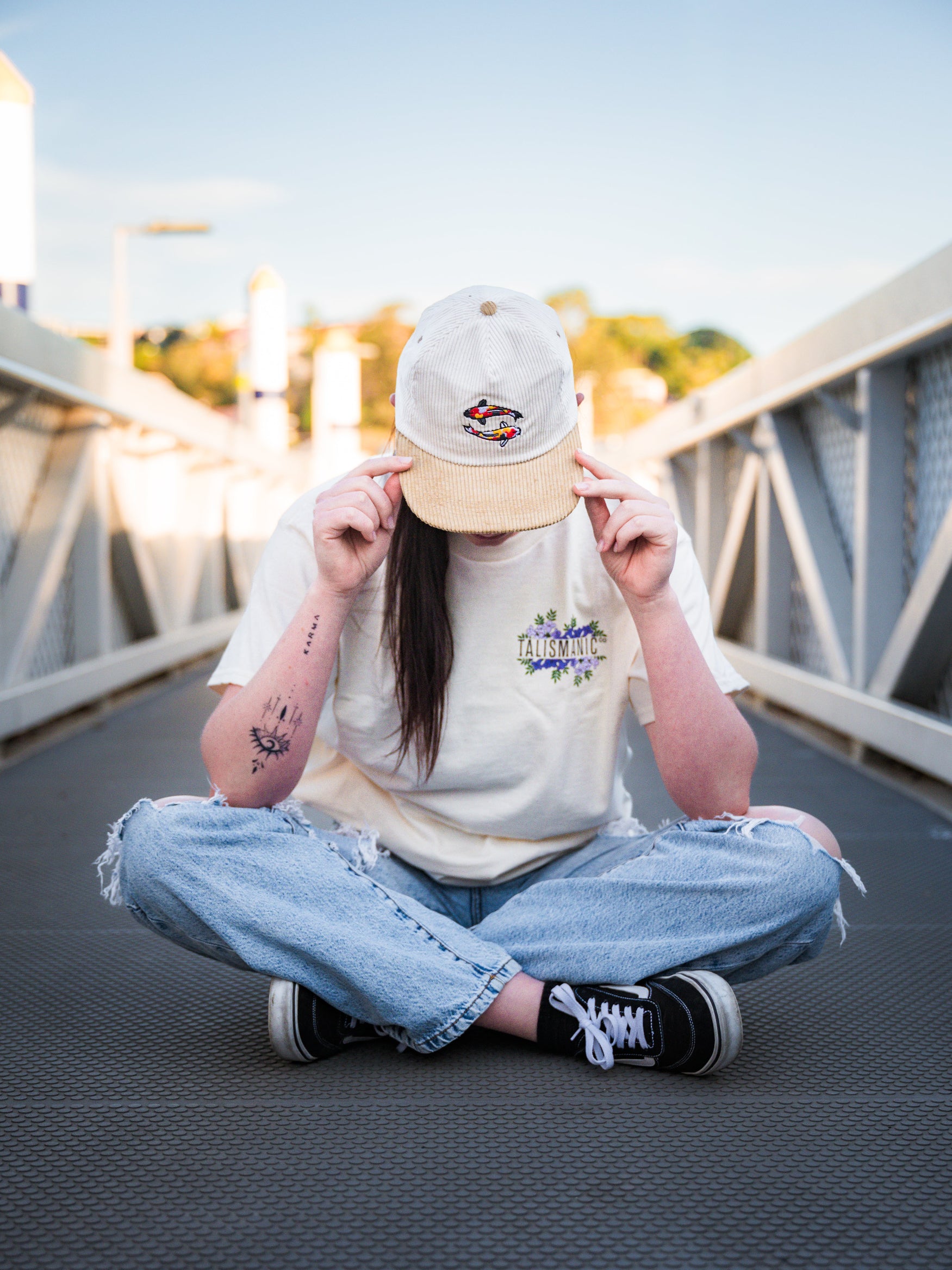 Person sitting on a bridge wearing koi fish corduroy cap and casual clothing