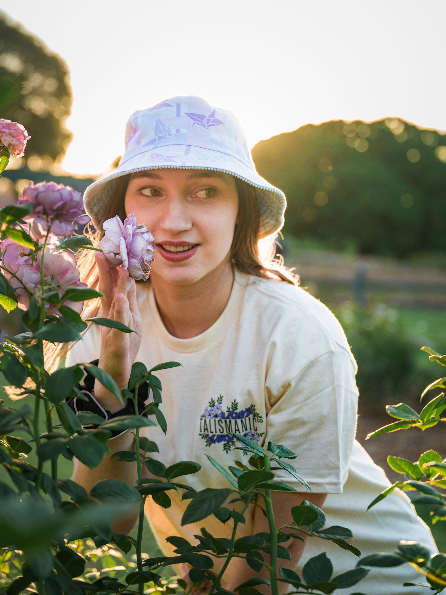 Person wearing a light-colored origami pattern bucket hat and floral shirt, surrounded by flowers